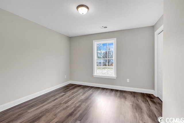 empty room with dark wood finished floors, visible vents, and baseboards