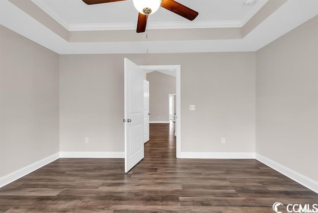 empty room featuring a tray ceiling, baseboards, wood finished floors, and crown molding