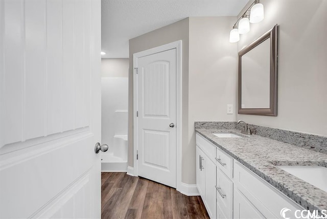 full bath featuring double vanity, a textured ceiling, wood finished floors, and a sink