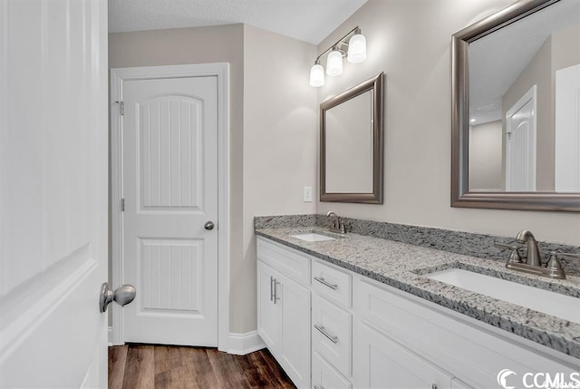 full bath featuring double vanity, wood finished floors, baseboards, and a sink