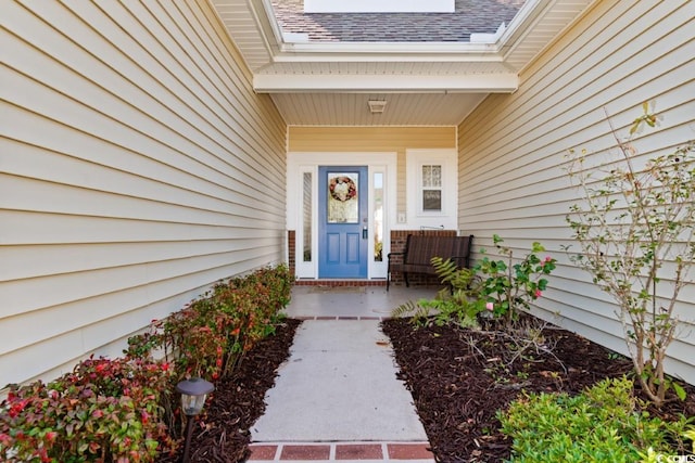 view of exterior entry featuring covered porch and a shingled roof