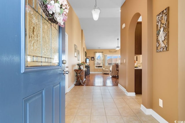 foyer featuring light tile patterned floors, ceiling fan, arched walkways, and baseboards