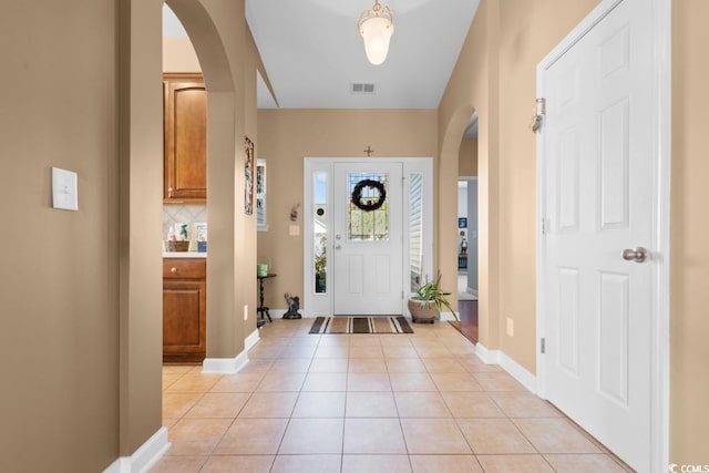 entrance foyer with light tile patterned floors, visible vents, arched walkways, and baseboards