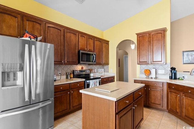 kitchen with a kitchen island, stainless steel appliances, arched walkways, light countertops, and light tile patterned floors