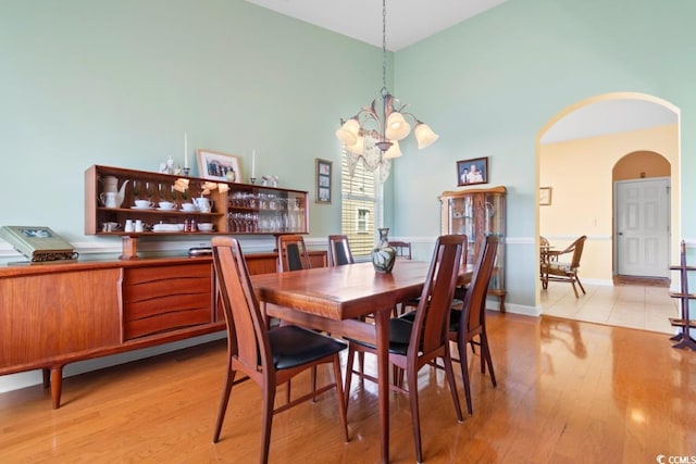 dining area with arched walkways, a chandelier, a high ceiling, and light wood-style floors