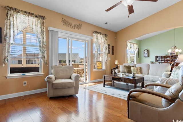 living area with visible vents, ceiling fan with notable chandelier, baseboards, and wood finished floors