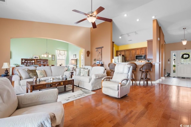 living room featuring track lighting, ceiling fan, light wood-style floors, arched walkways, and high vaulted ceiling