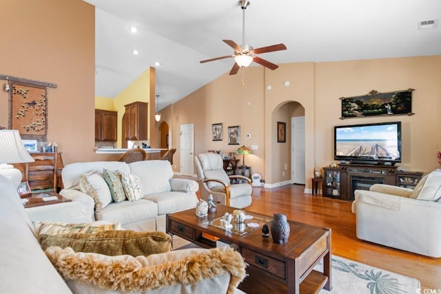 living area featuring visible vents, high vaulted ceiling, a ceiling fan, arched walkways, and light wood-style floors