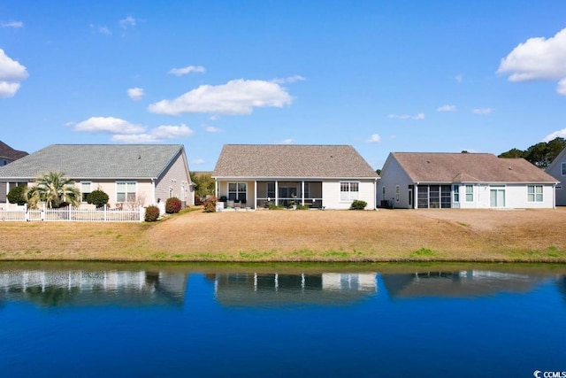 back of property featuring fence, a sunroom, a yard, and a water view