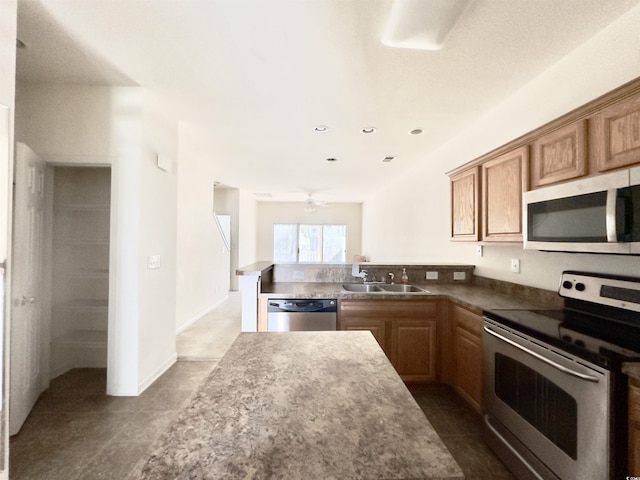 kitchen featuring brown cabinets, appliances with stainless steel finishes, a peninsula, a ceiling fan, and a sink