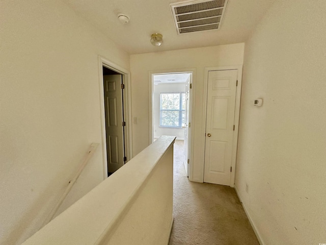 hallway with visible vents, an upstairs landing, light colored carpet, and baseboards