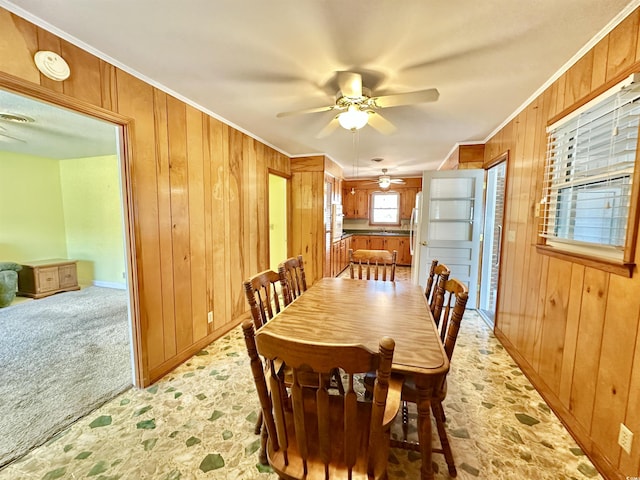 dining area featuring ceiling fan, light colored carpet, wood walls, and ornamental molding