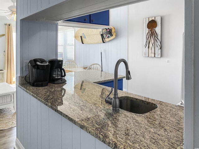 kitchen featuring a sink, blue cabinetry, wood finished floors, stone counters, and ceiling fan