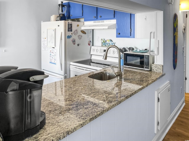 kitchen with blue cabinetry, under cabinet range hood, dark wood finished floors, white appliances, and a sink