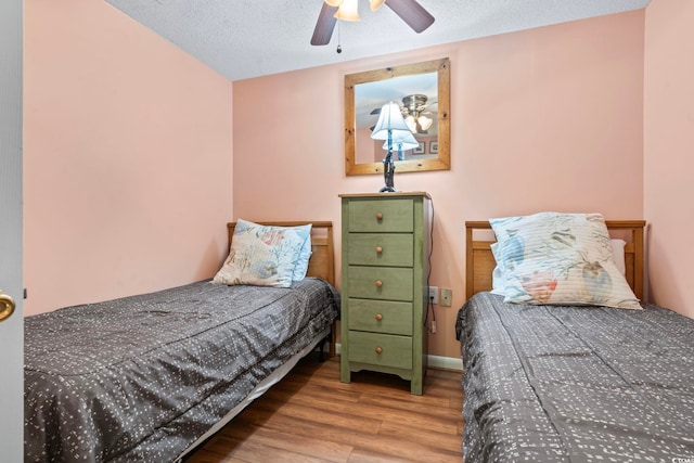 bedroom with ceiling fan, wood finished floors, baseboards, and a textured ceiling