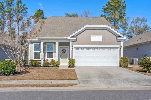 view of front facade with cooling unit, an attached garage, driveway, and roof with shingles