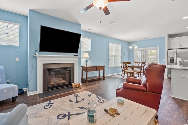 living room featuring a glass covered fireplace, baseboards, dark wood finished floors, and ceiling fan with notable chandelier