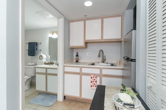 kitchen with light tile patterned floors, freestanding refrigerator, a sink, light countertops, and white cabinets