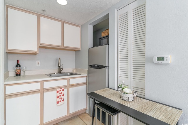 kitchen with light countertops, freestanding refrigerator, a textured ceiling, white cabinetry, and a sink