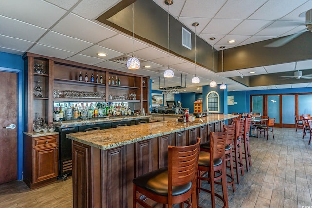 bar featuring indoor wet bar, a drop ceiling, light wood-style flooring, and a ceiling fan