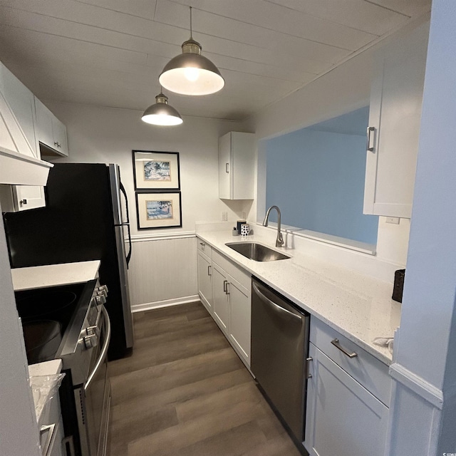 kitchen with a wainscoted wall, a sink, appliances with stainless steel finishes, white cabinets, and dark wood-style flooring