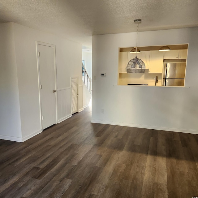 unfurnished living room featuring dark wood finished floors, stairway, baseboards, and a textured ceiling