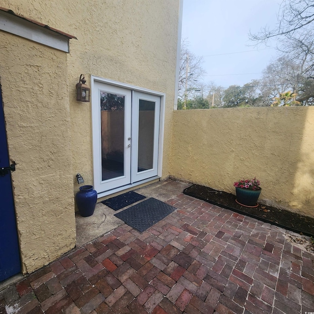 entrance to property with stucco siding, french doors, a patio, and fence