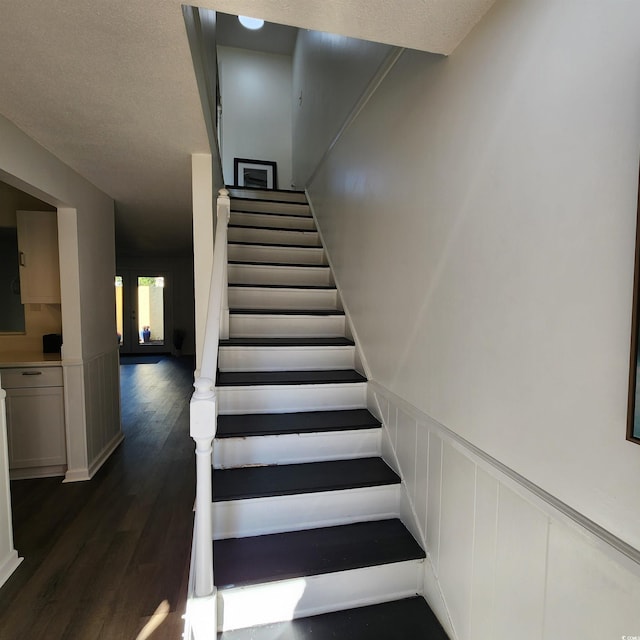 staircase featuring a decorative wall, a textured ceiling, a wainscoted wall, and wood finished floors