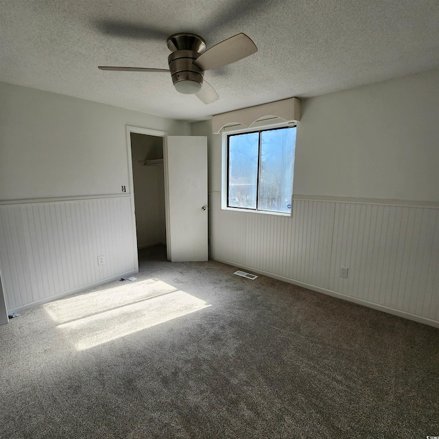 unfurnished bedroom with visible vents, a textured ceiling, and a wainscoted wall