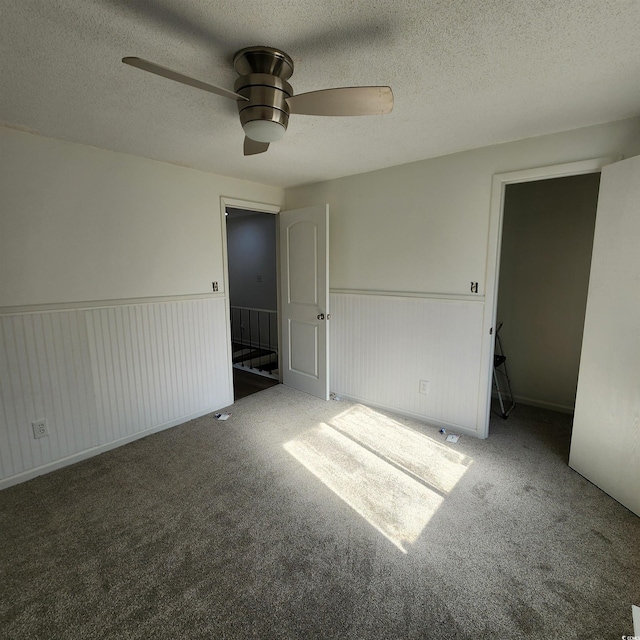 unfurnished bedroom featuring a wainscoted wall, carpet, a ceiling fan, and a textured ceiling