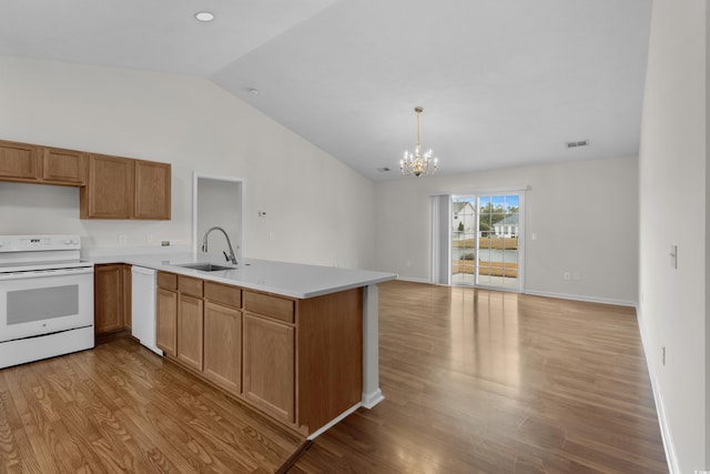 kitchen featuring white appliances, wood finished floors, visible vents, a peninsula, and a sink