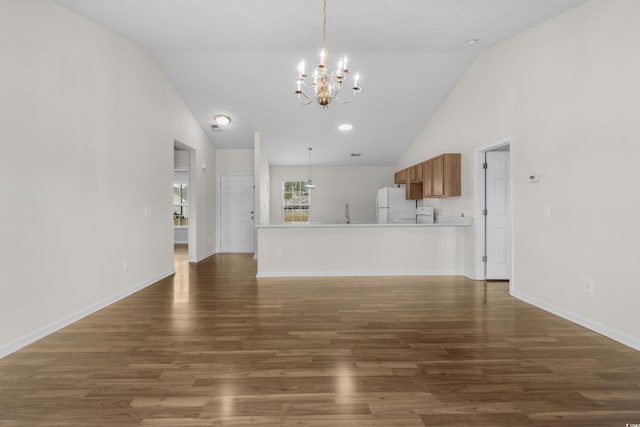 unfurnished living room with high vaulted ceiling, a sink, wood finished floors, an inviting chandelier, and baseboards