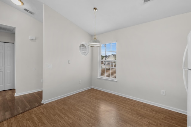 unfurnished dining area featuring vaulted ceiling, visible vents, baseboards, and wood finished floors