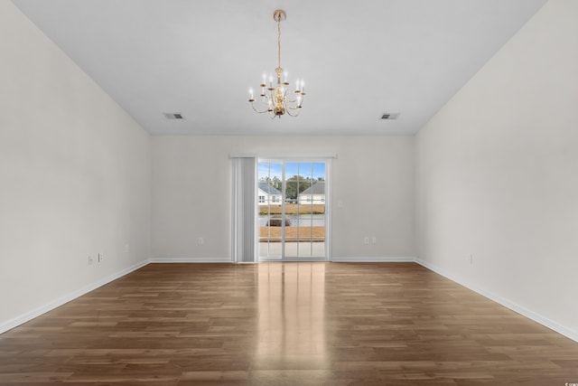 spare room featuring visible vents, baseboards, an inviting chandelier, and wood finished floors