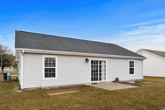 rear view of property featuring cooling unit, a lawn, roof with shingles, and a patio area