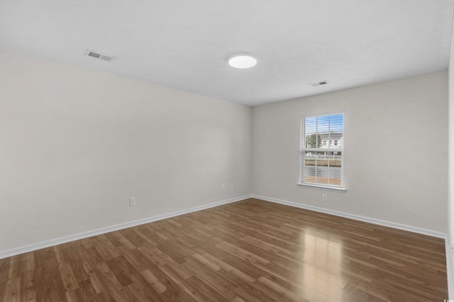 empty room featuring visible vents, baseboards, and wood finished floors