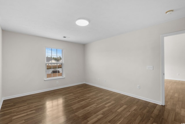 spare room featuring visible vents, dark wood-type flooring, and baseboards