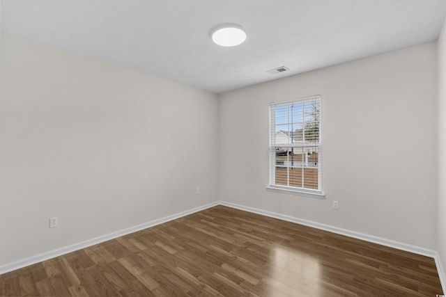 empty room with visible vents, dark wood-type flooring, and baseboards