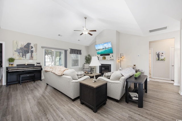 living area featuring light wood finished floors, visible vents, ceiling fan, vaulted ceiling, and a glass covered fireplace