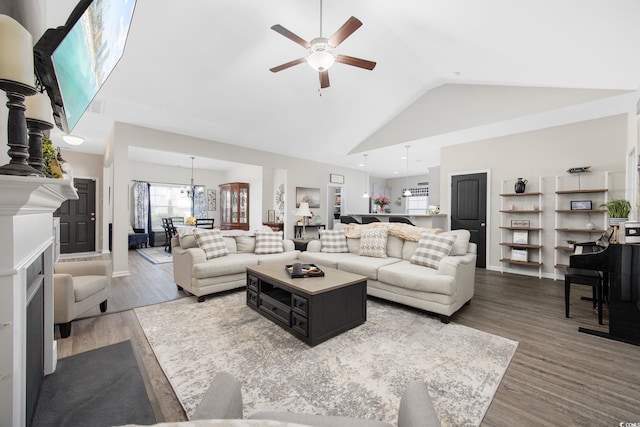 living area with ceiling fan with notable chandelier, high vaulted ceiling, and wood finished floors