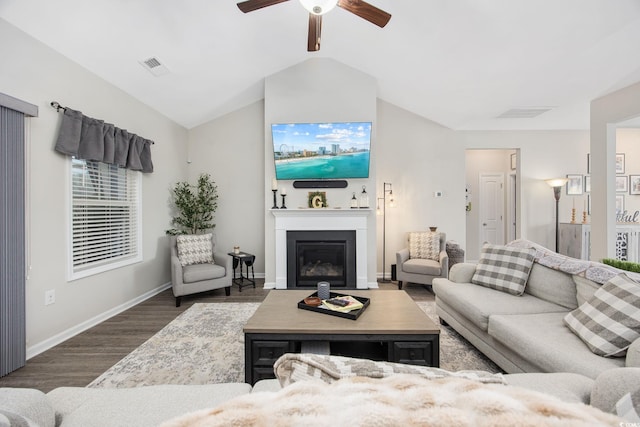 living room featuring wood finished floors, visible vents, baseboards, lofted ceiling, and a glass covered fireplace