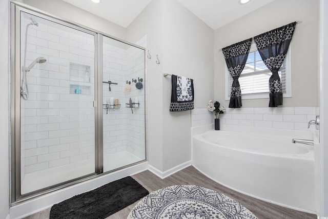 bathroom featuring a bath, wood finished floors, a stall shower, and baseboards