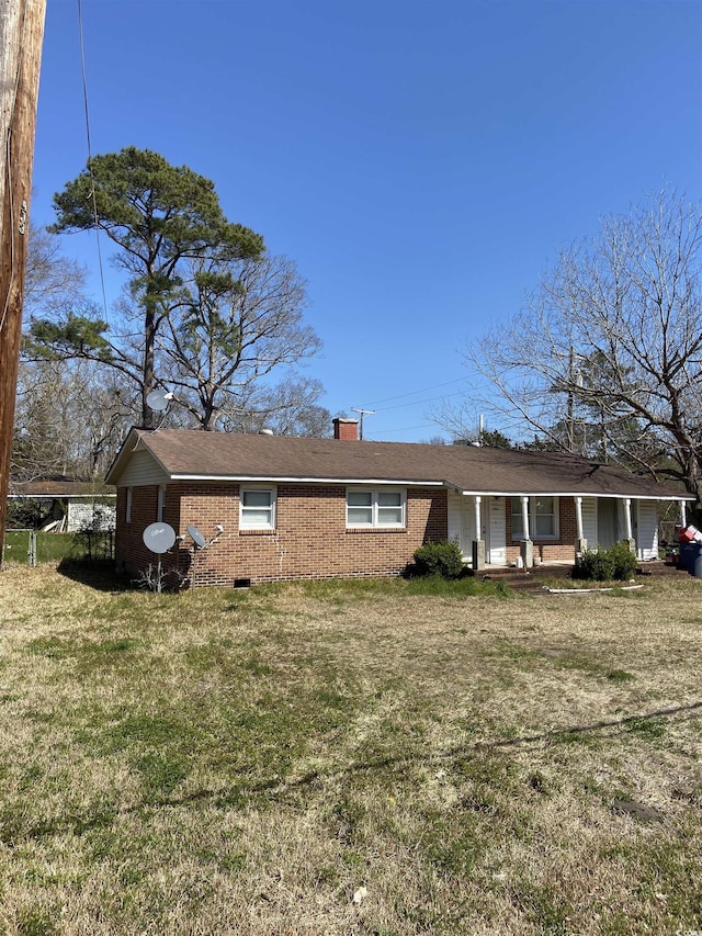 rear view of property featuring a porch, a lawn, brick siding, and a chimney