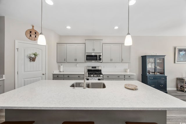 kitchen with gray cabinetry, a center island with sink, light countertops, appliances with stainless steel finishes, and a sink