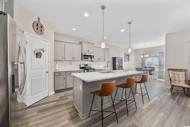 kitchen featuring a breakfast bar, gray cabinetry, a sink, appliances with stainless steel finishes, and light wood finished floors