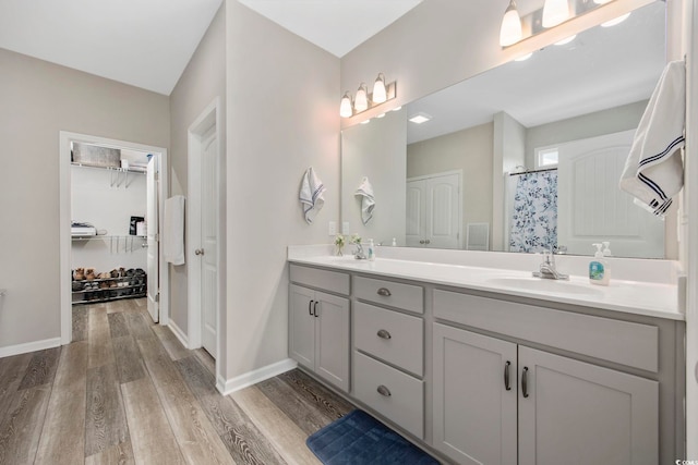 bathroom featuring a sink, wood finished floors, double vanity, baseboards, and a spacious closet