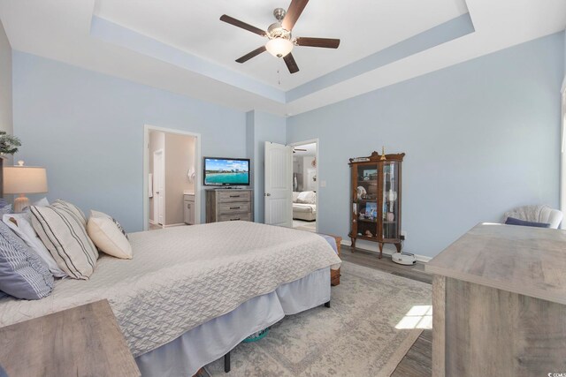 bedroom with ceiling fan, baseboards, wood finished floors, ensuite bath, and a raised ceiling