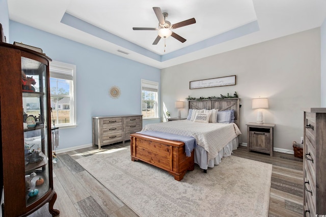 bedroom featuring visible vents, a raised ceiling, wood finished floors, baseboards, and ceiling fan