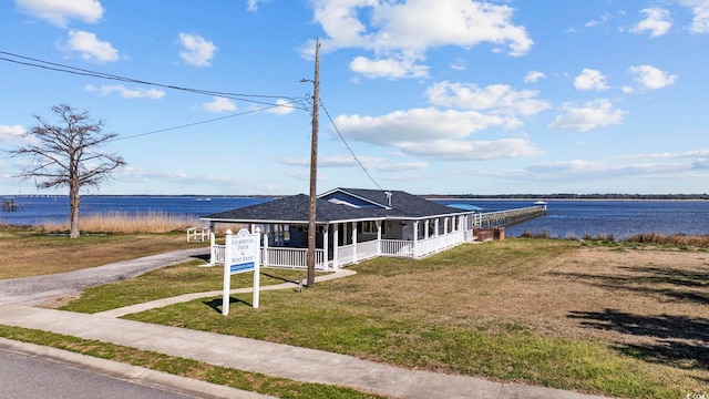 view of front of house featuring driveway, covered porch, a shingled roof, a front lawn, and a water view