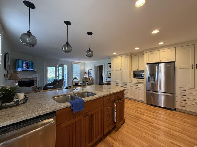 kitchen with recessed lighting, a sink, stainless steel appliances, a brick fireplace, and light wood-type flooring